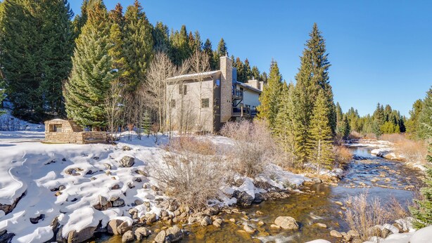 A lodge with a stone exterior, a stone chimney, and a view of a flowing river surrounded by snow and trees. - Walk to Ski Lift: Breckenridge Retreat w/ 2 Decks! (Breckenridge)