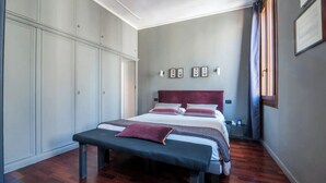 Une chambre à coucher comprenant un lit, un banc, une armoire et des lampes fixées au mur.