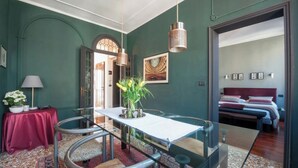 Un coin repas avec une table en verre, des chaises et un vase de fleurs. La pièce adjacente contient un lit avec une tête de lit et des oreillers.