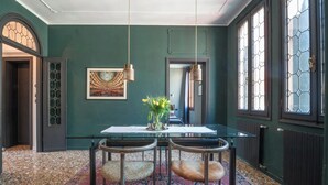 Un coin repas avec une table en verre, deux chaises, un vase de fleurs et un tableau au mur.