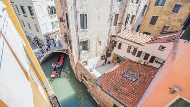 Un canal étroit où glisse une gondole, bordé de bâtiments historiques dotés de balcons et surmonté d’un pont.