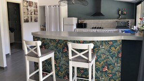 Uma cozinha com uma ilha curva, cadeiras brancas, micro-ondas, torradeira e luminária pendente.