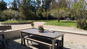 Um pátio externo com mesa e banco de madeira, rodeado por cascalho e vegetação.