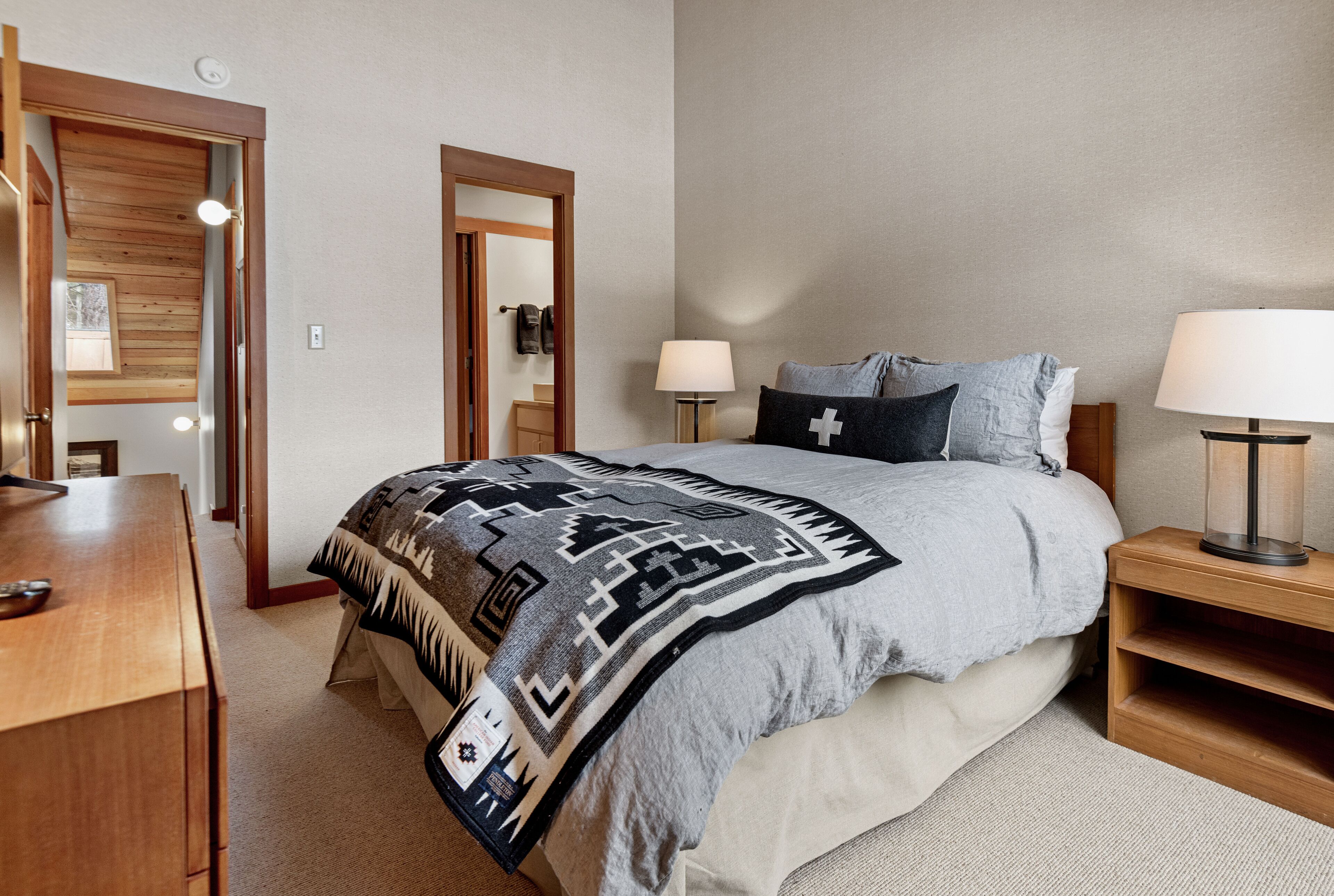 Une chambre à coucher comprenant un lit, des tables de chevet, une commode en bois et un miroir.