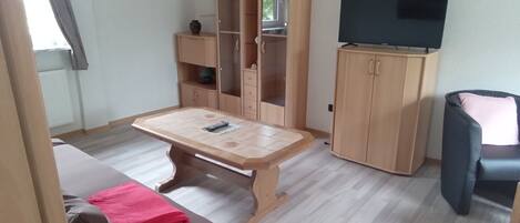 Una sala de estar con una mesa de madera, un sofá, un mueble para televisión y una silla negra.