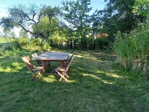 Conjunto de mesa e cadeiras de madeira em área externa gramada, com árvores ao fundo.