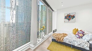 A modern bedroom with a large window, a bed with patterned bedding, and a colorful abstract painting on the wall. - A Lux & Cozy Apt Next to Southern Cross Station (Melbourne)