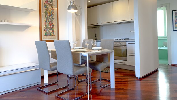 A modern kitchen with white cabinets, a stainless steel stove, and a dining area with a table set for two. - New Bright and Quiet in the Heart of Trastevere (Roma)
