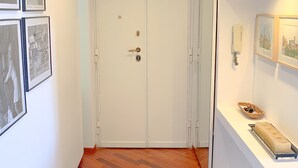 A hallway with a wooden floor, a white door with a keyhole, and framed pictures on the walls. - New Bright and Quiet in the Heart of Trastevere (Roma)