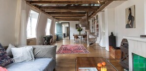 A cozy living room with a sofa, a coffee table with oranges and a magazine, a red rug, and a fireplace with green tiles. - ON THE BANKS OF SEINE-AN EXPLICIT 17TH CENT.TOWNHOUSE LE MARAIS VILLAGE ST PAUL (Paris)
