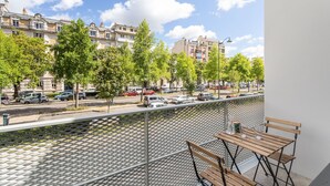A balcony with a view of a street lined with trees and parked cars, overlooking a row of buildings. - Moines - Appartement moderne et confortable (Rennes)