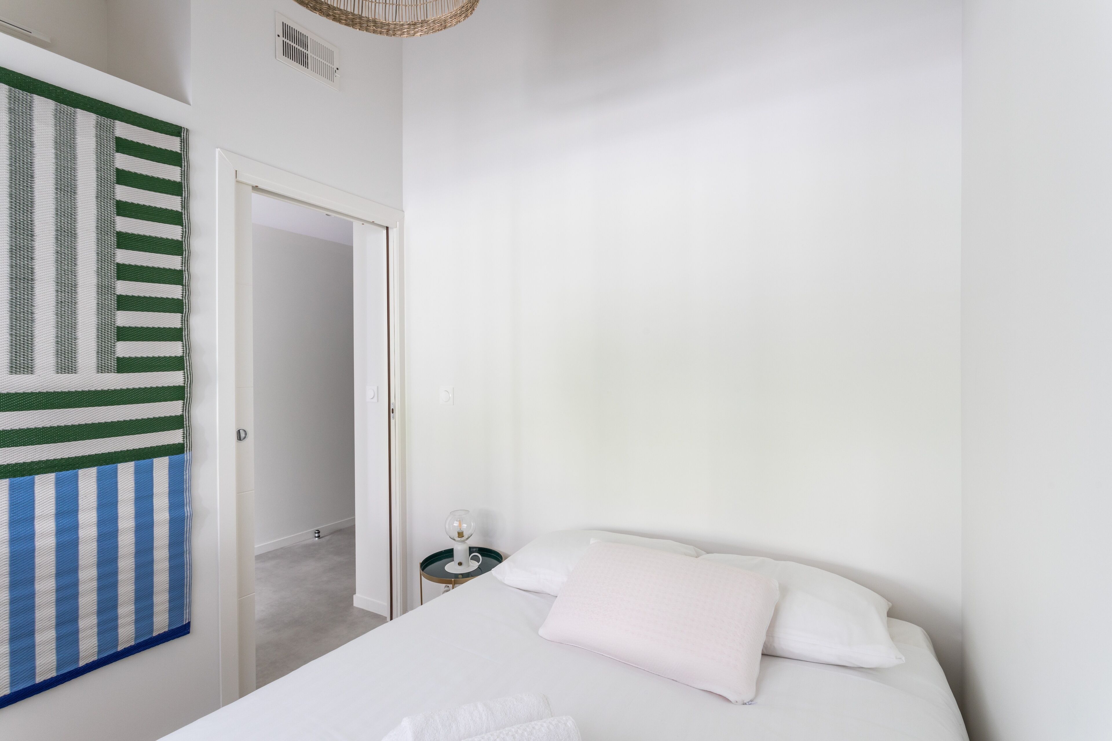Een slaapkamer met een bed, een nachtkastje, een lamp en een groen-wit gestreepte handdoek aan de muur.