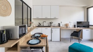 A modern kitchen with white cabinets, a dining area with a wooden table, and a TV on a wooden desk. - Moines - Appartement moderne et confortable (Rennes)