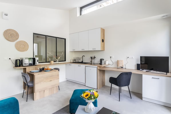 A modern kitchen with white cabinets, a wooden countertop, and a built-in microwave. There is a large window above the sink, and a flat-screen TV mounted on the wall. - Moines - Appartement moderne et confortable (Rennes)