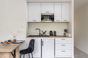 Een compacte keuken met witte kastjes, een ingebouwde magnetron, een spoelbak en een kleine koelkast.