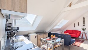 A compact, modern apartment with a kitchenette, dining area, and living space. It features skylights, a red sofa, and a small refrigerator. - Teranga - Studio avec grande terrasse dans Rennes (Rennes)