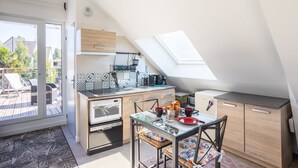 A compact kitchen with a skylight, a dining area with a glass table, and a view of the outside deck. - Teranga - Studio avec grande terrasse dans Rennes (Rennes)