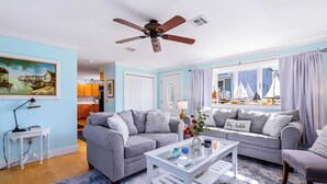 A living room with a ceiling fan, two grey sofas, a white coffee table, and a view of boats through a window. - Luxury 2-Story PTown Condo: 5 Min Walk to Commercial St. Private Patio & Parking (Provincetown)