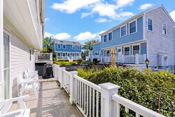 A residential area with a wooden deck, white railings, and houses with blue and white siding.