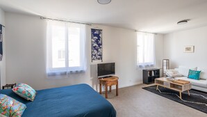 Ein Schlafzimmer mit einem Bett, einem Fernseher, einem Holznachttisch, einer Couch und einem schwarzen Teppich.