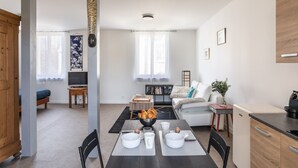 Ein modernes Wohnzimmer mit Esstisch für zwei Personen, einer Couch, einem Fernseher und einem Bücherregal.