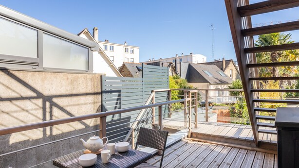 Ein Balkon mit Tisch, der für Tee gedeckt ist, einem Stuhl und Blick auf benachbarte Gebäude.