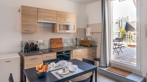 Eine moderne Küche mit Holzschränken, einer schwarzen Arbeitsplatte und einem Essbereich mit Tisch für zwei Personen.