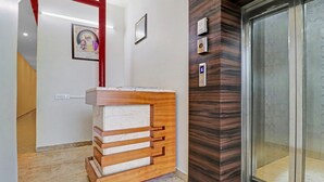 A reception desk with a marble top and wooden slats, a red pillar, and a wall-mounted alarm clock. - Itsy Hotels Jashan (Mohali)