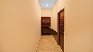 A narrow hallway with beige walls and a carpeted floor, leading to a wooden door with a modern design. - Itsy Hotels Jashan (Mohali)