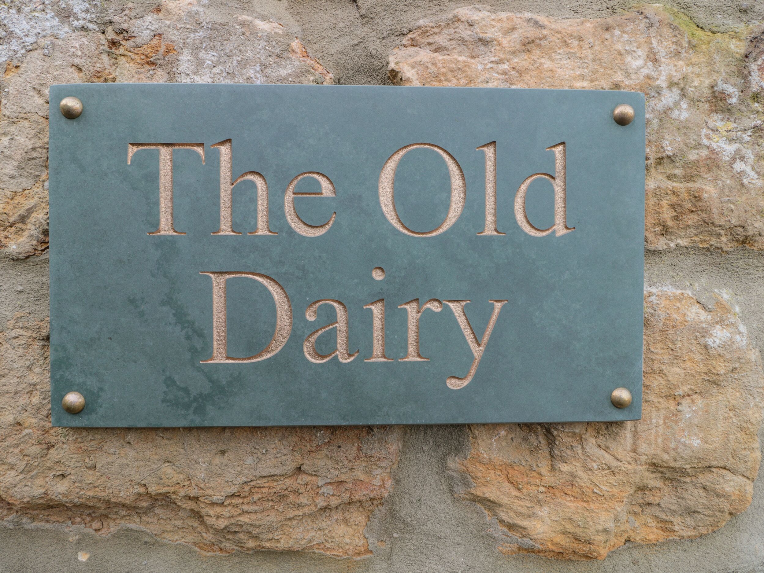 A sign with the text "The Old Dairy" mounted on a stone wall.