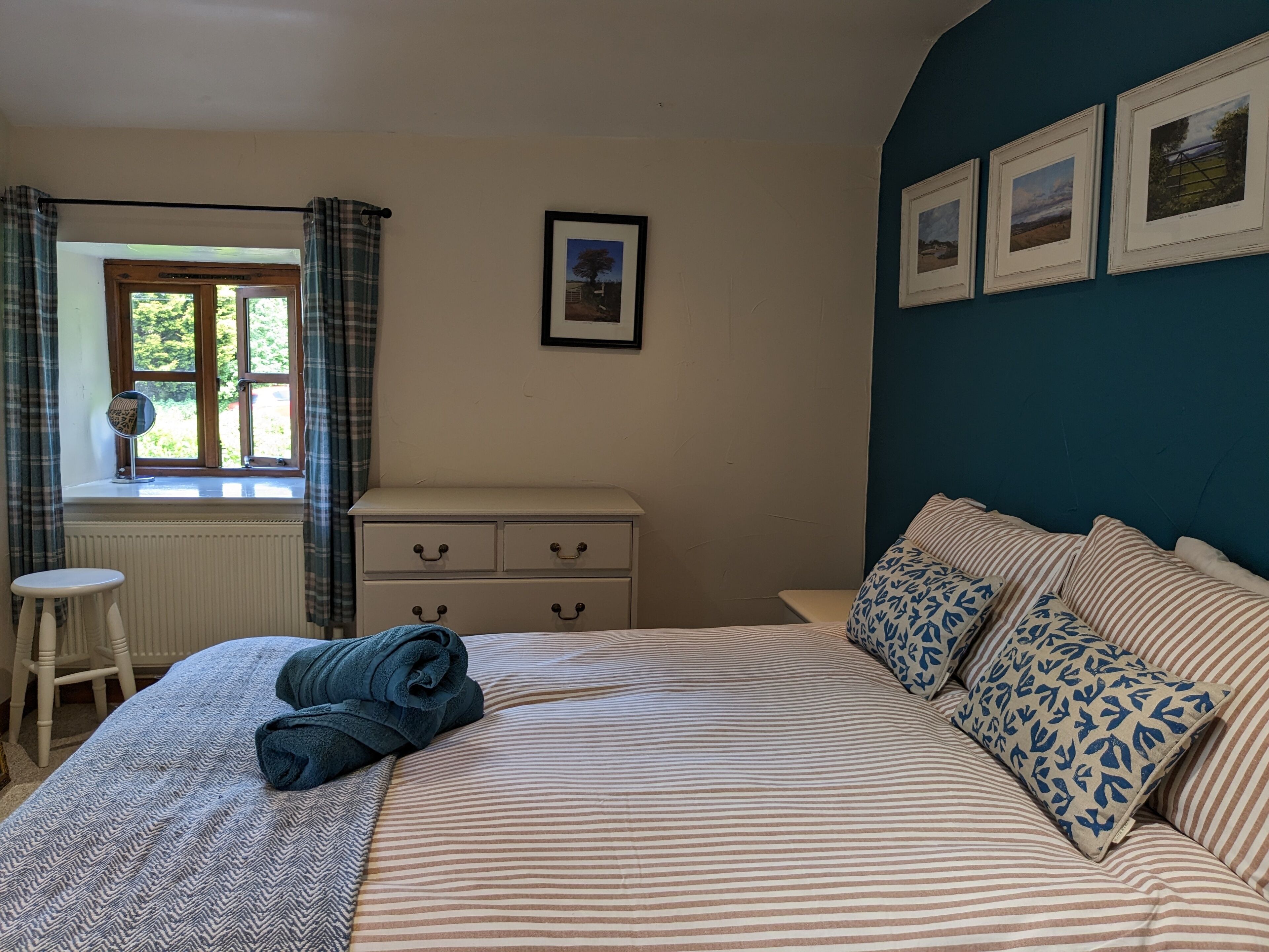 A bedroom with a bed, a dresser, a window with curtains, and framed pictures on the wall.