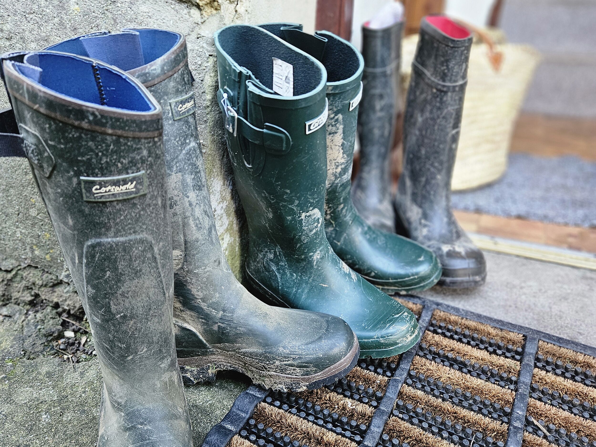 A pair of green rubber boots with a label, placed on a doormat.