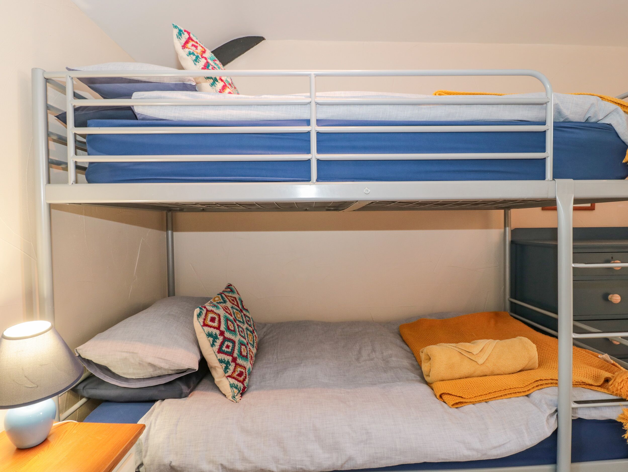 Ein Etagenbett mit Schreibtisch und Lampe, ein Kissen mit Muster und eine gefaltete Decke.