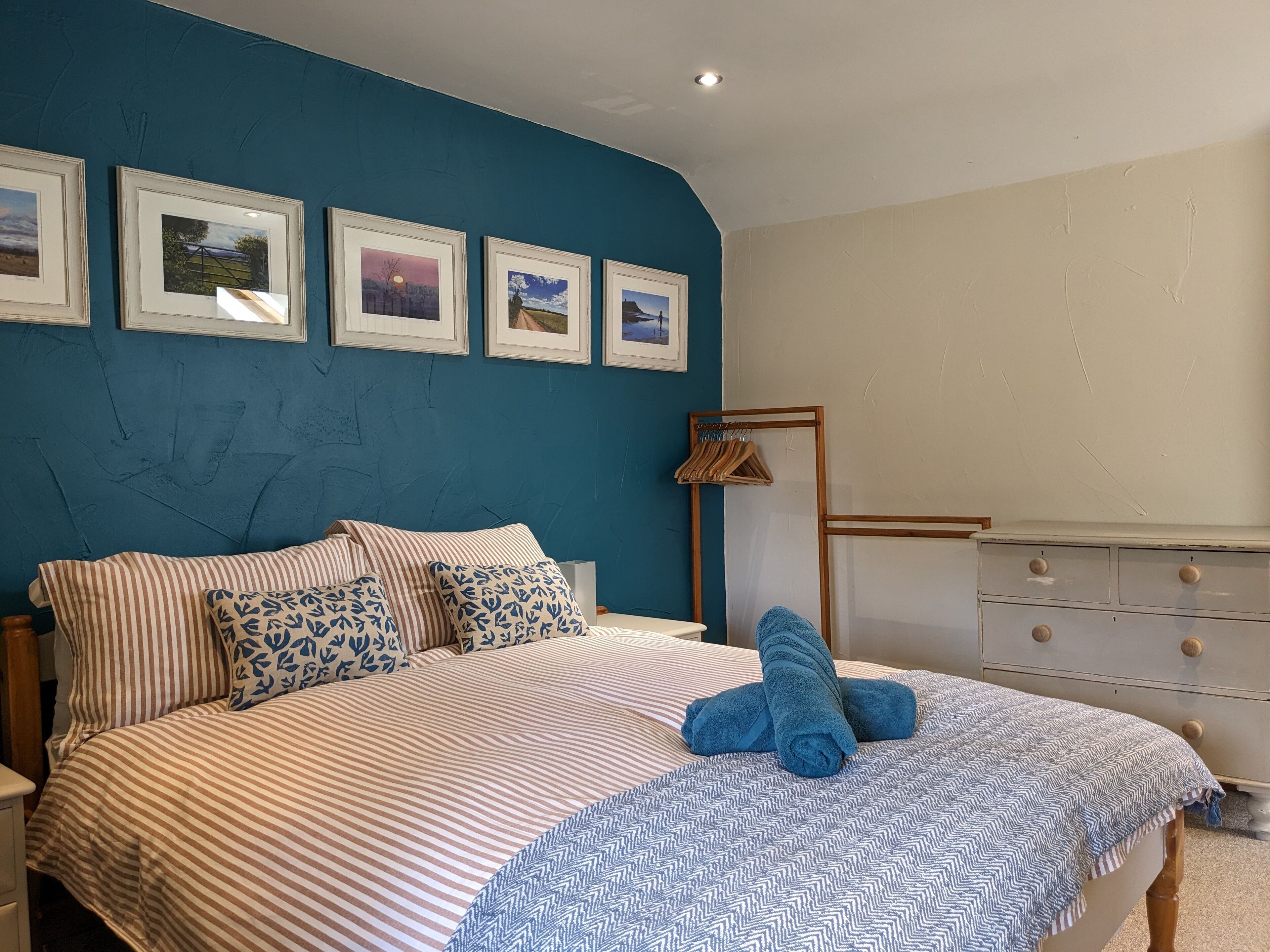 A bedroom with a bed, a dresser, and four framed pictures on the wall.