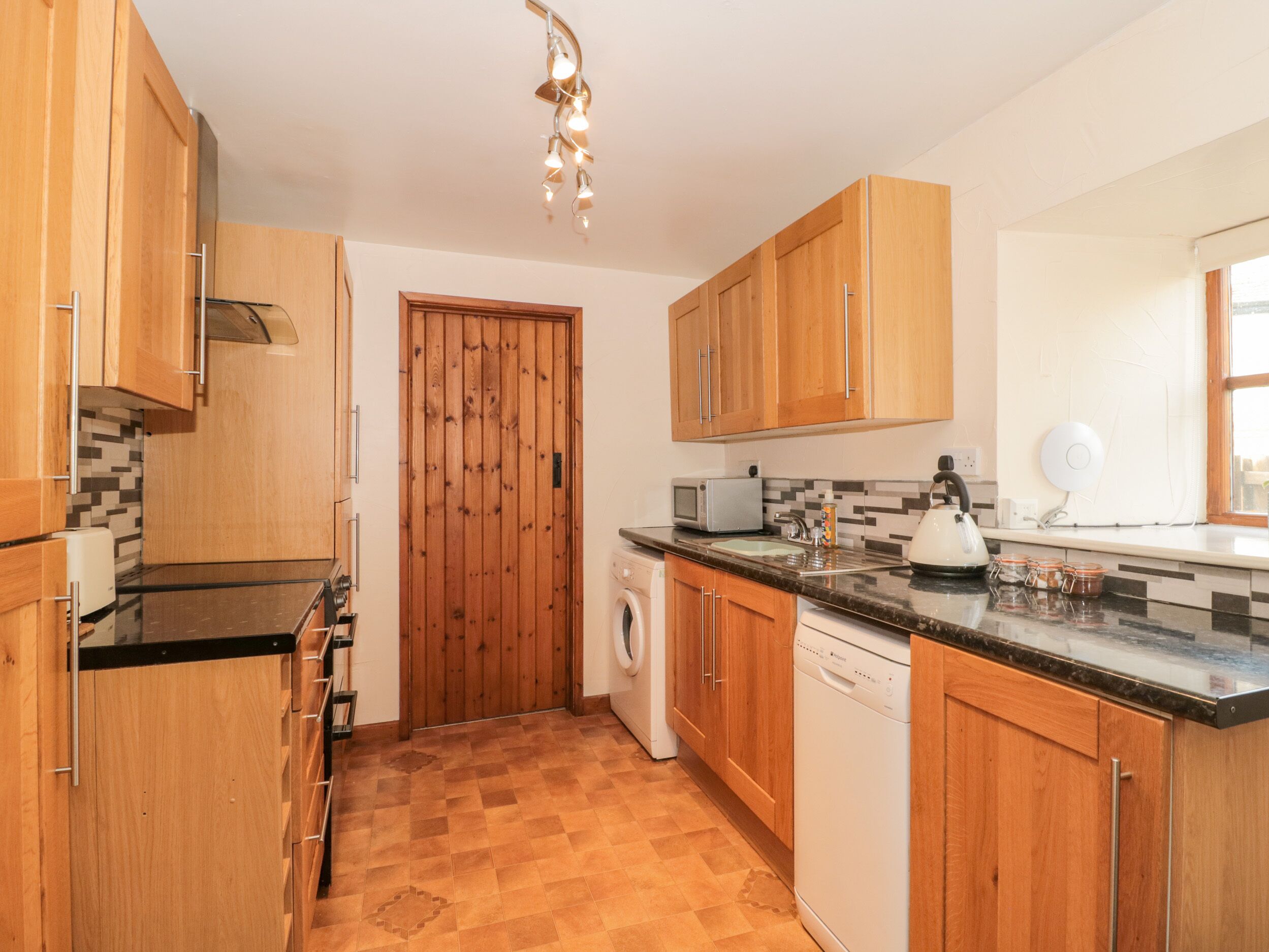 A kitchen with wooden cabinets, a microwave, a kettle, and a washing machine.