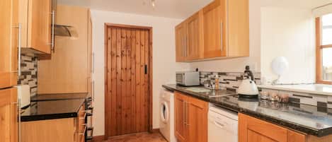 A kitchen with wooden cabinets, a microwave, a kettle, and a washing machine.