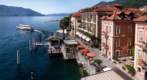 A waterfront hotel with a stone dock, outdoor seating, and a view of the lake and mountains. - Hotel Cannero Lakeside Resort (Cannero Riviera)