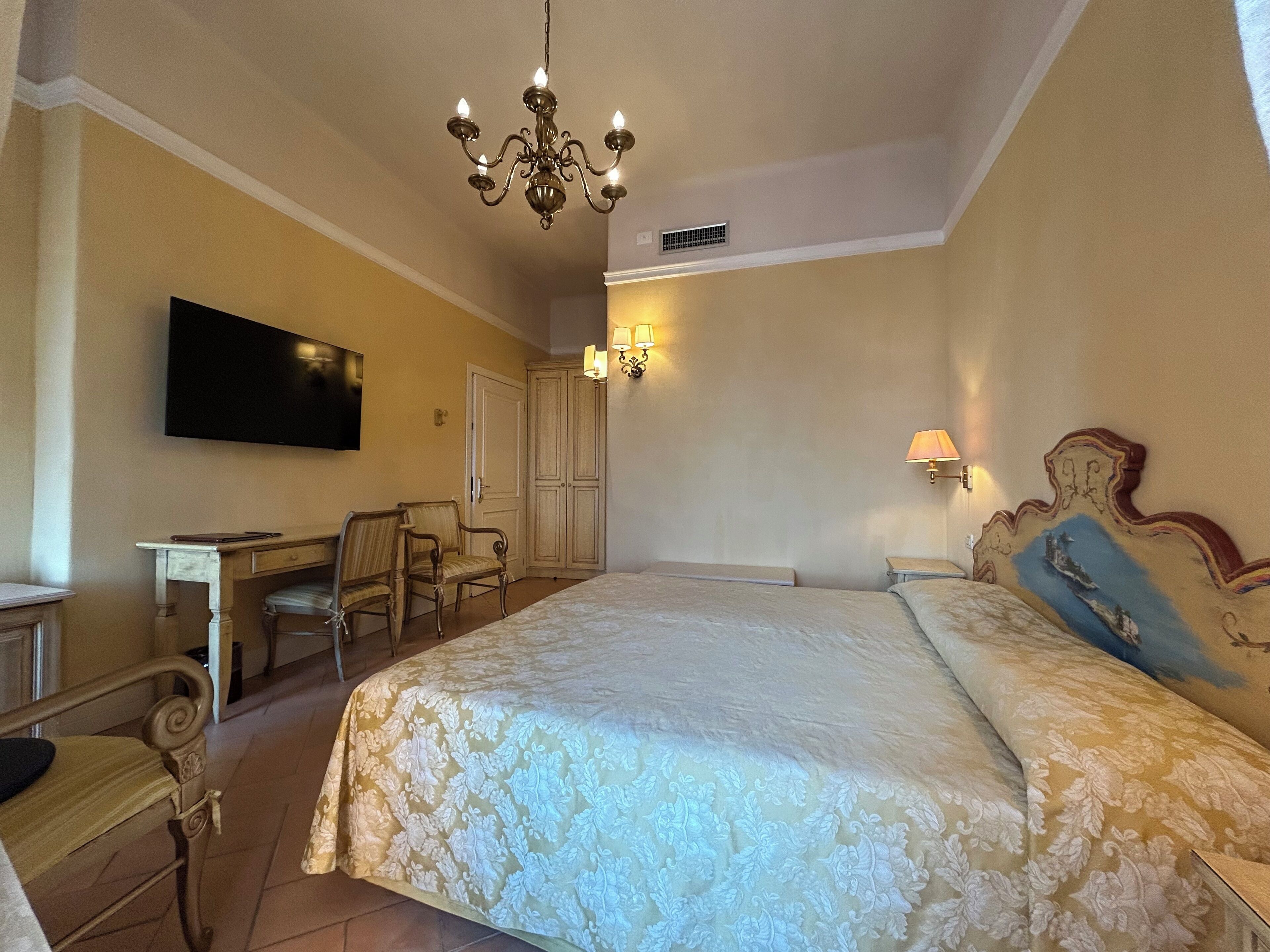 Una habitación de hotel con una cama grande, un escritorio con una silla, un televisor y una araña.