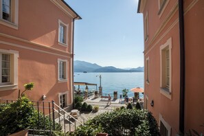 A view of a lakeside terrace with buildings, outdoor seating, and a clear sky. - Hotel Cannero Lakeside Resort (Cannero Riviera)