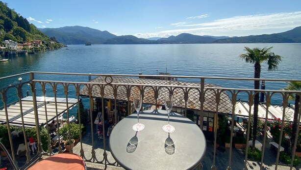 Eine Terrasse mit Tischen und Stühlen mit Blick auf einen See, im Hintergrund Berge.