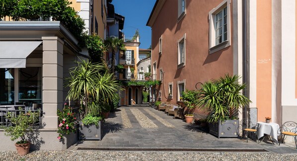 A narrow street with buildings on either side, outdoor seating, and potted plants.