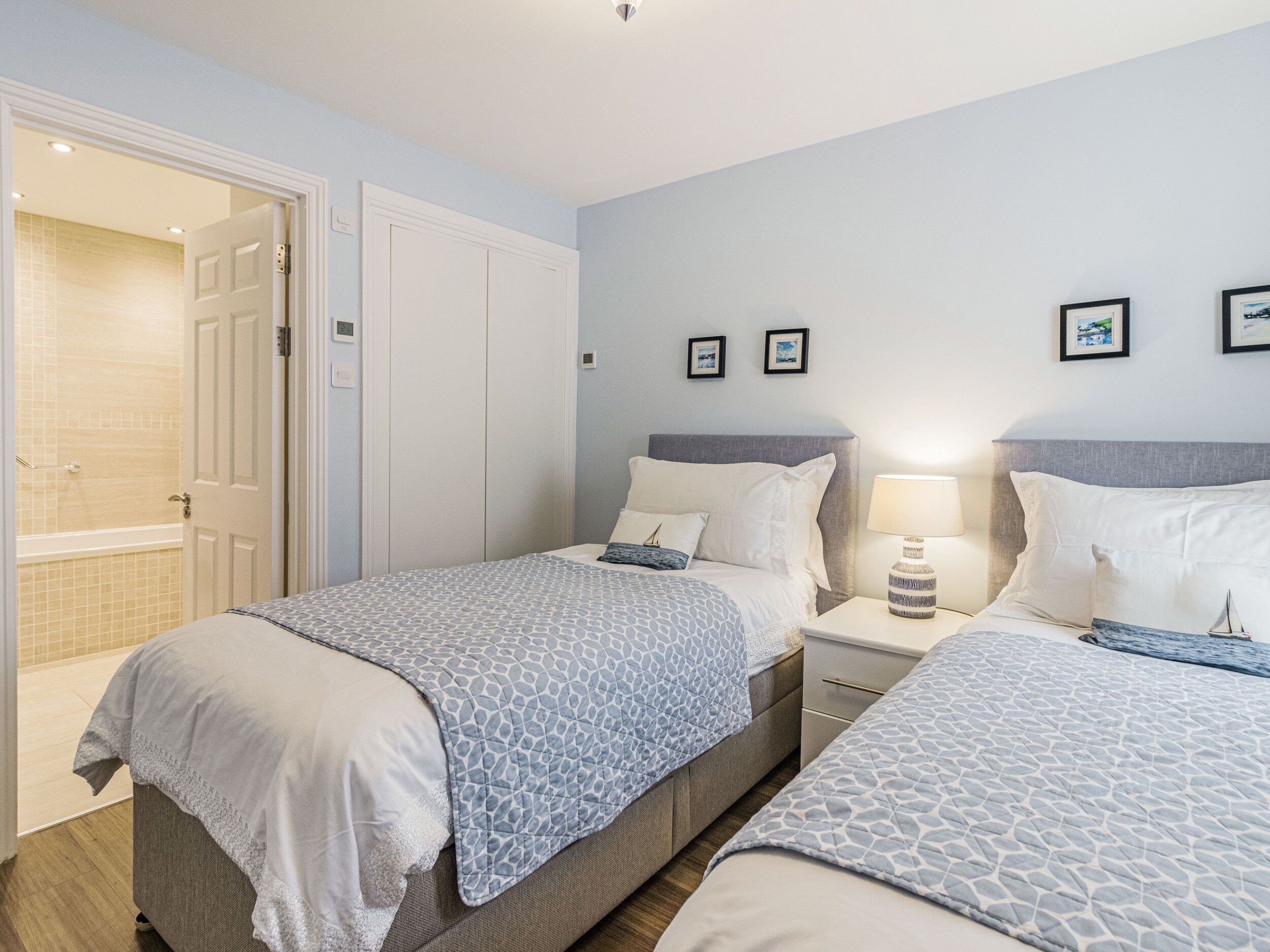 A hotel room with two beds, a bathroom with a shower, and a small bedside table with a lamp.