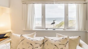 Une pièce dotée d’une grande fenêtre donnant sur une plage, avec une sculpture d’oiseau posée sur le rebord de la fenêtre.