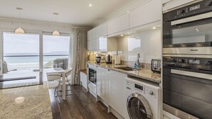 Une cuisine moderne dotée d’un four encastré, d’un lave-linge et d’un coin repas offrant une vue sur la mer.
