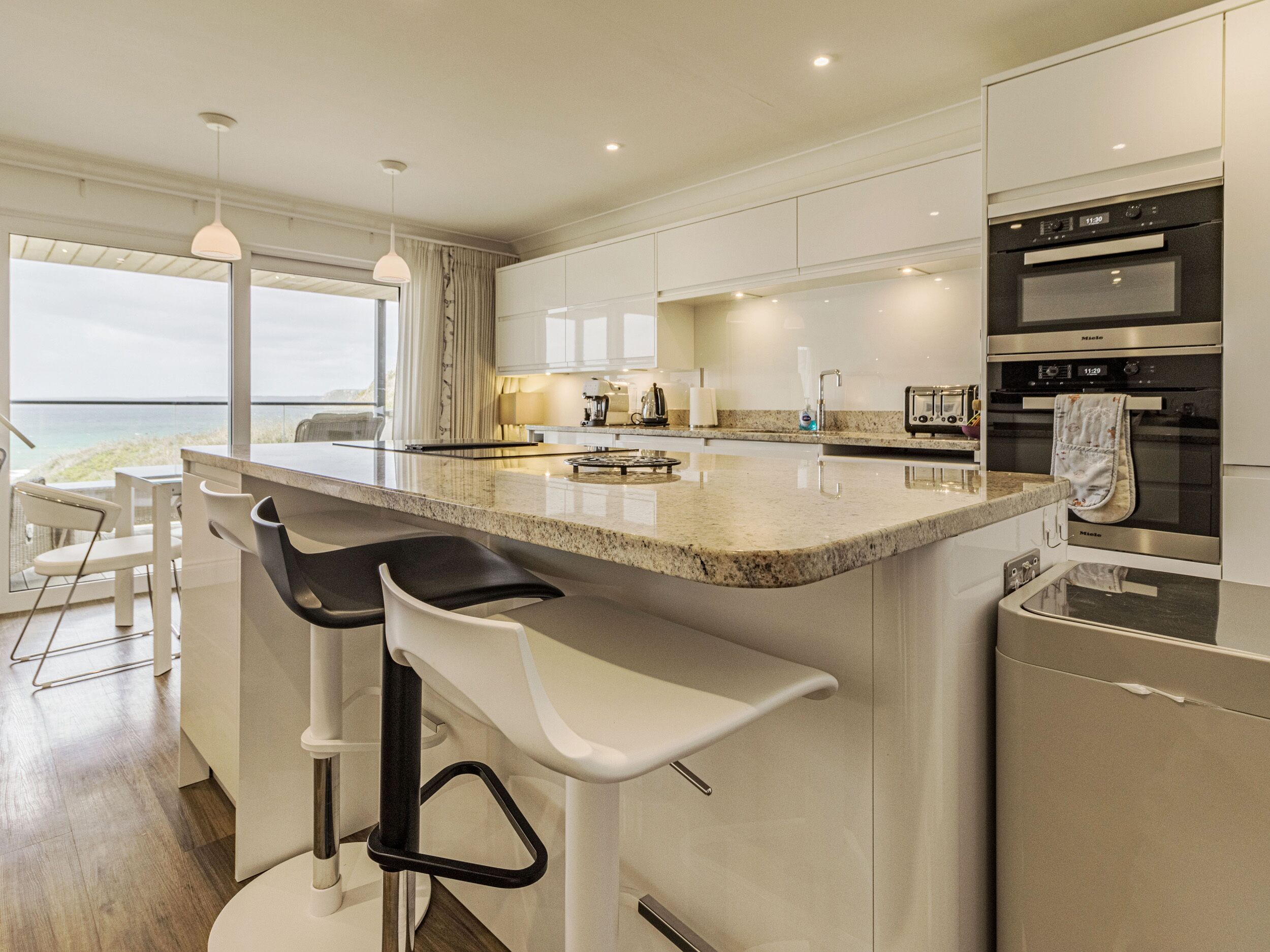 A modern kitchen with a large island, bar stools, and a view of the ocean.