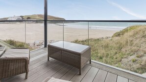 Un balcon doté de meubles en osier, offrant une vue sur une plage et un bâtiment situé au loin.