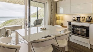 Une cuisine moderne avec des meubles blancs, un coin repas doté d’une table en verre et une vue sur l’océan.