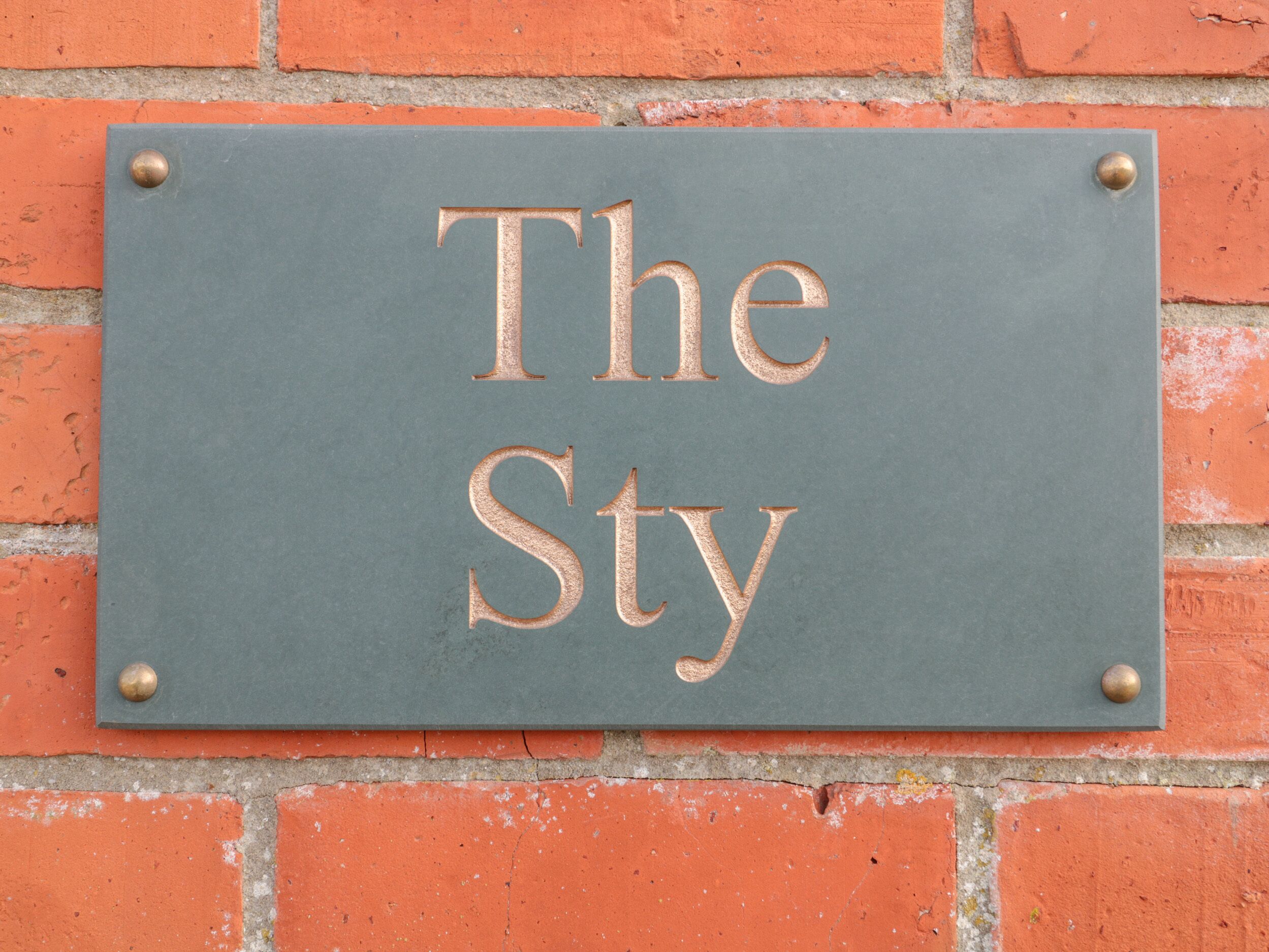 A sign with the words "The Sty" mounted on a brick wall.