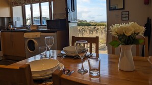 A dining area with a table set for two, a washing machine, a microwave, and a view of the outdoors. - The Sty (Bridport)