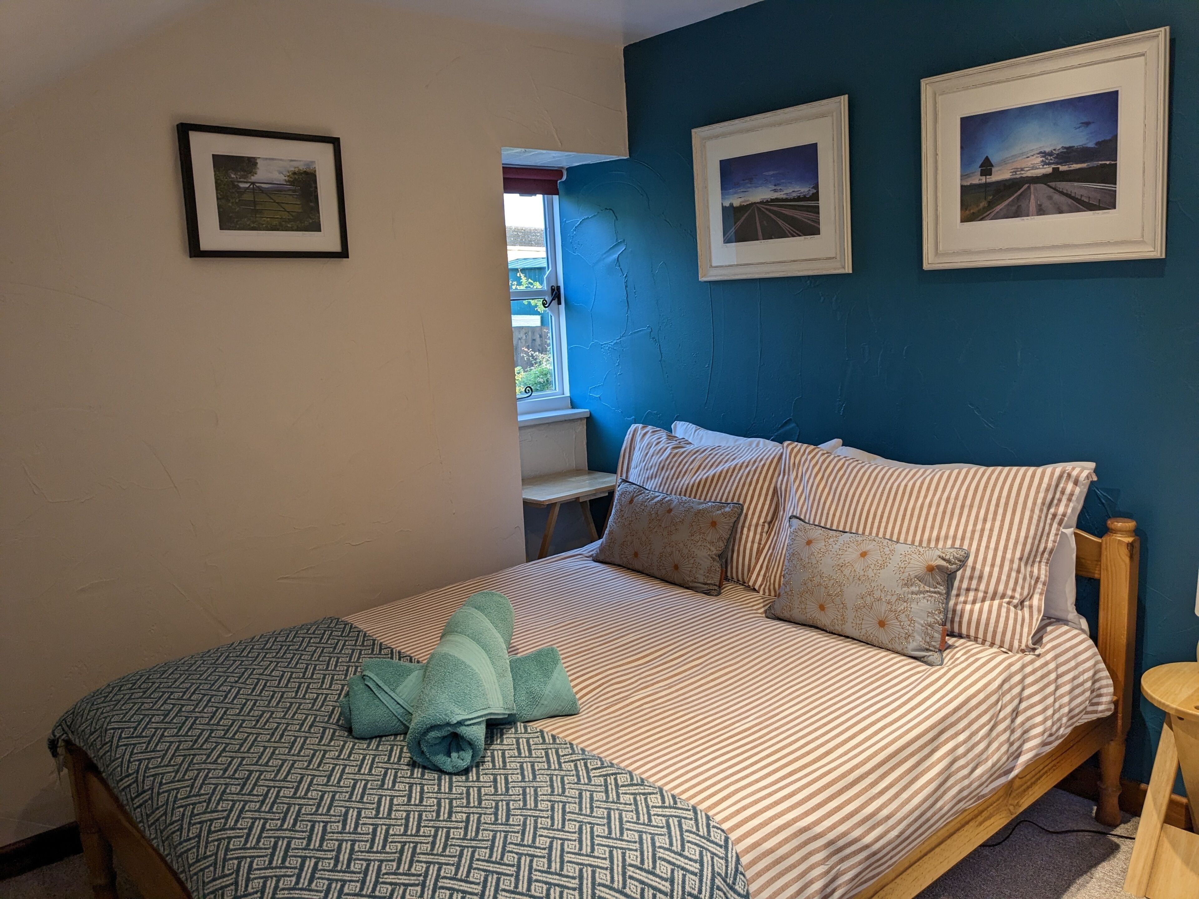 A bedroom with a bed, pillows, a window, and two framed pictures on the wall.